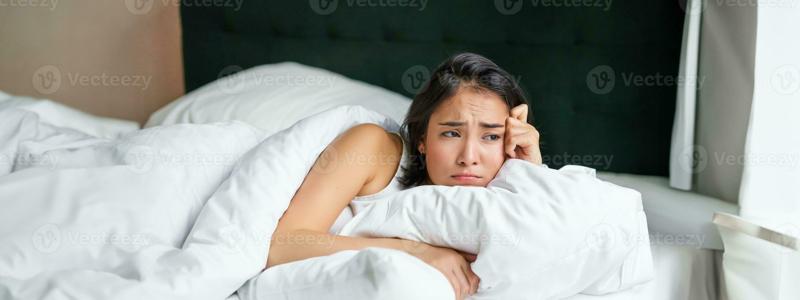 triste et sombre asiatique fille mensonge dans sa lit, grimaçant et pleurs, sentiment bouleversé, dépenses temps dans sa chambre à coucher, étreindre oreiller photo