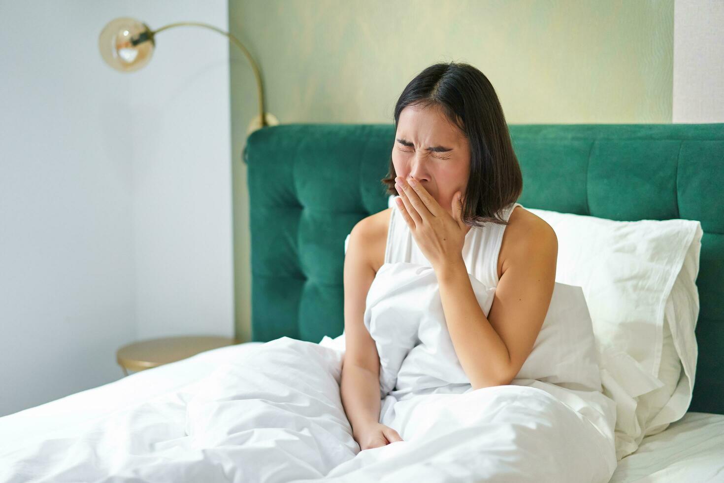 femme veille en haut dans lit, bâillement et grimaçant, de bonne heure Matin après dormir, séance dans chambre photo