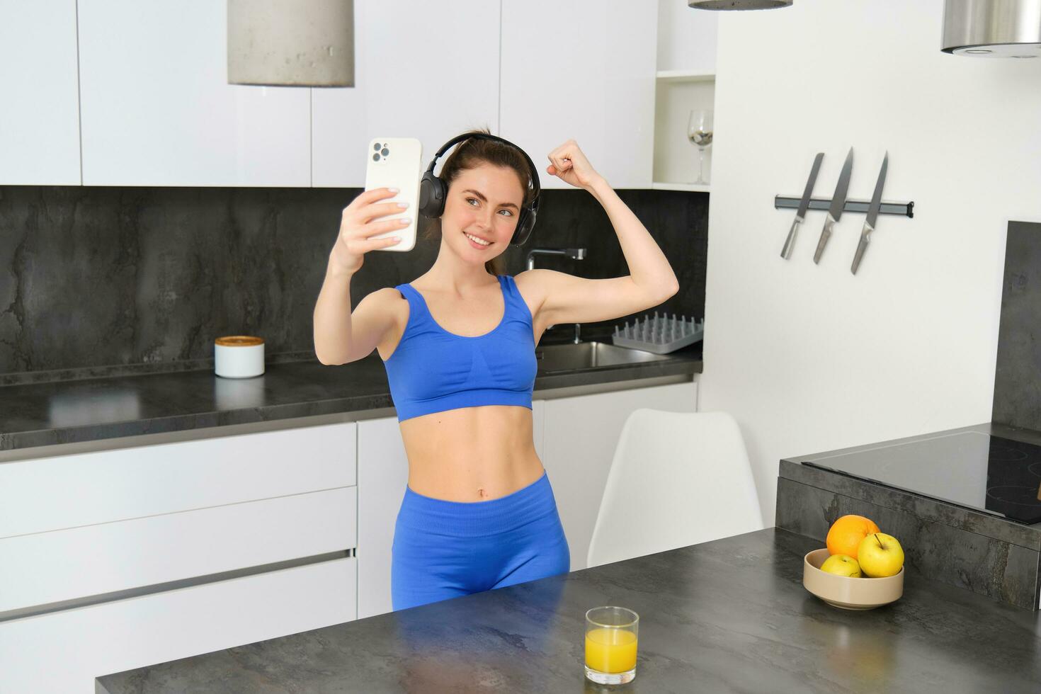 portrait de magnifique Jeune femme blogueur, prise selfie dans sa faire des exercices vêtements, spectacles sa muscles, fléchissement biceps sur téléphone intelligent caméra, enregistrements vidéo pour social médias photo