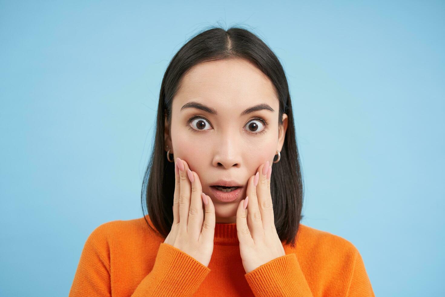 proche en haut portrait de asiatique fille avec sous le choc affronter, regards à qch incroyable, surpris par nouvelles, des stands plus de bleu Contexte photo