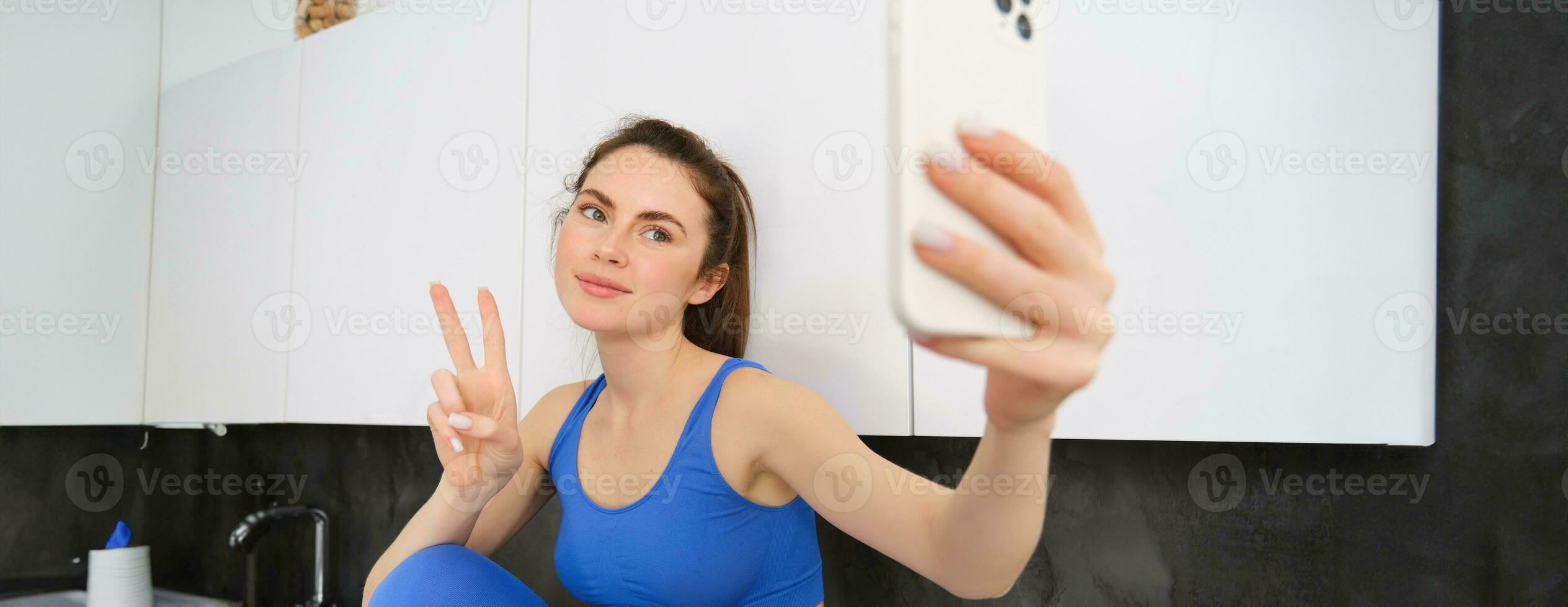 en forme et en bonne santé Jeune des sports femme, montrant paix signe, prise selfie dans vêtements de sport, aptitude blogueur fabrication Photos pour social médias dans sa vêtements de sport