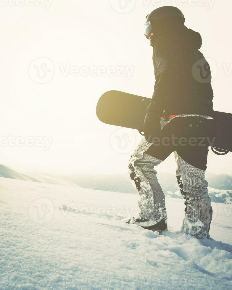 snowboarder marchant avec snowboard au coucher du soleil dans les montagnes enneigées. fond cinématographique de snowboarder freerider solo photo