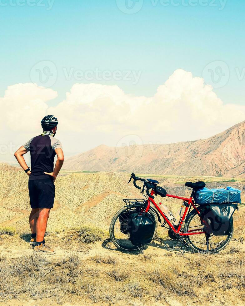 vue arrière statique cycliste masculin caucasien debout près d'un vélo de randonnée rouge regardant sur fond de montagnes pittoresques. concept de mode de vie actif et inspirant photo