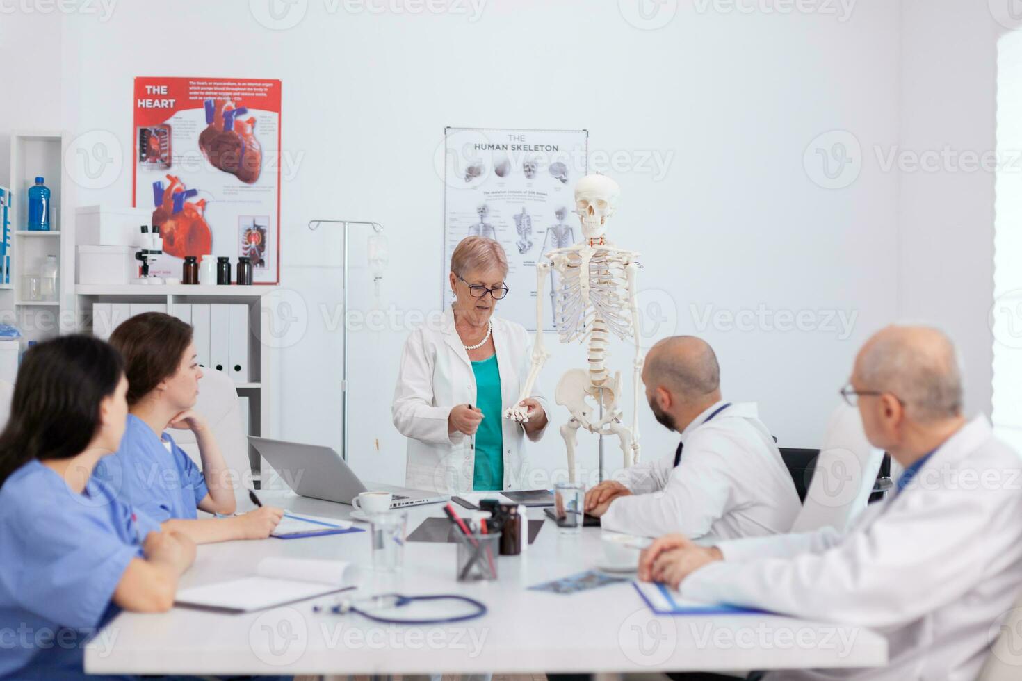 médecin Sénior femme en portant OS structure discuter Humain structure en utilisant corps squelette en présentant soins de santé traitement. hôpital groupe travail à médical compétence dans réunion pièce photo