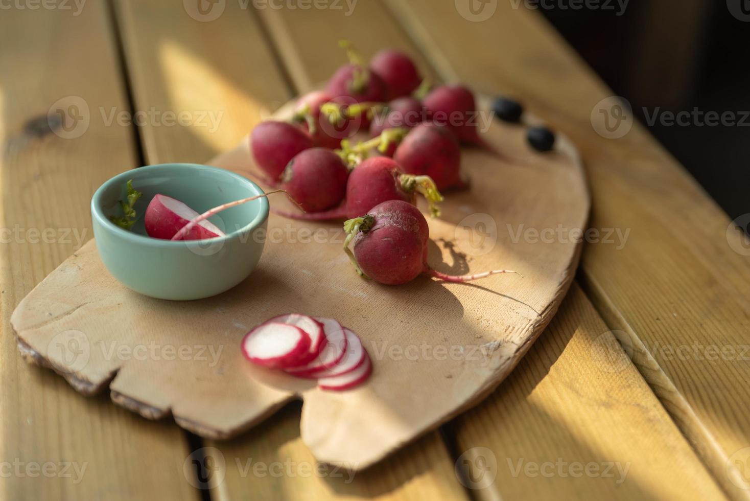 le soleil de l'après-midi brille sur la plaque en bois, radis rouge complet et tranché photo