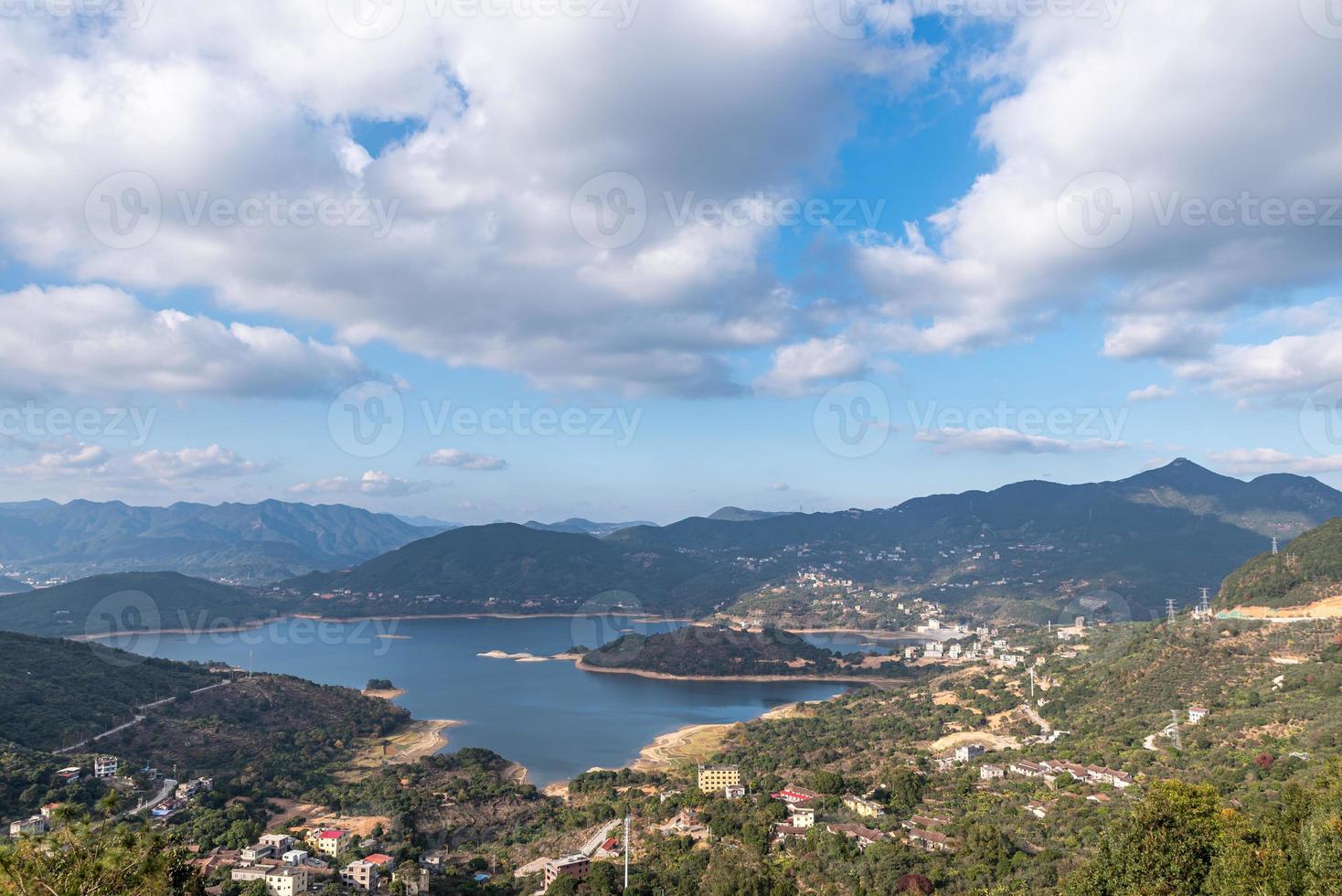 le réservoir sous le ciel bleu et les nuages blancs est entouré de montagnes et de forêts photo