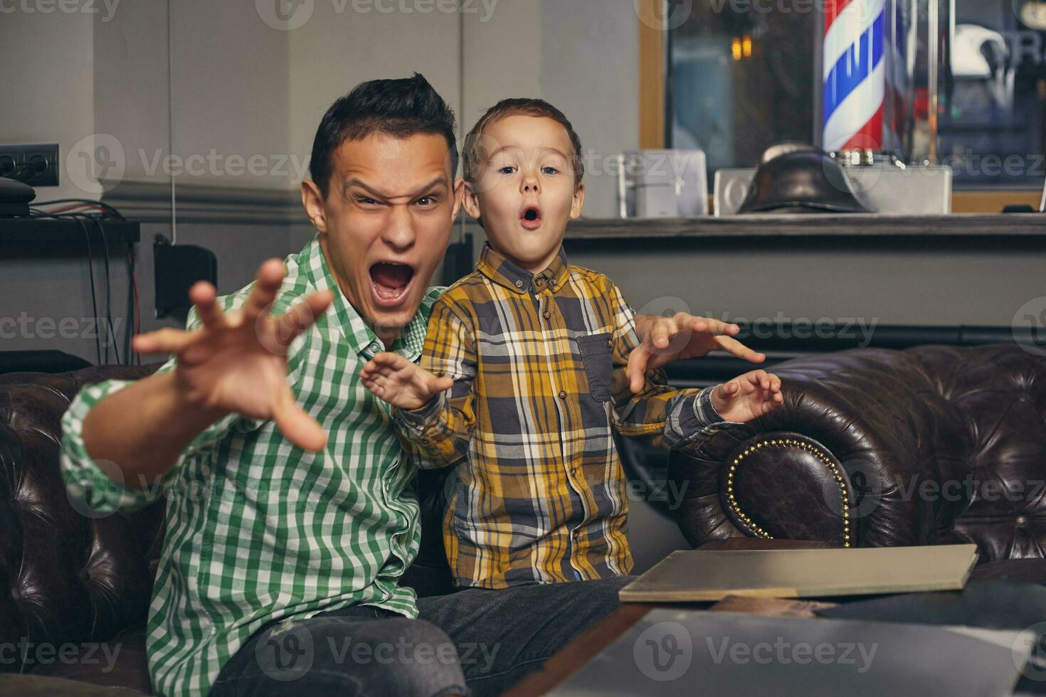 Jeune père et le sien élégant peu fils dans le salon de coiffure dans le attendre chambre. photo