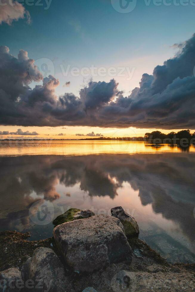 parfait le coucher du soleil sur le rivages de Lac gooimer près Almere. le violet-orange enfer illumine le qui passe des nuages et reflète sur le calme surface. beauté de Pays-Bas photo