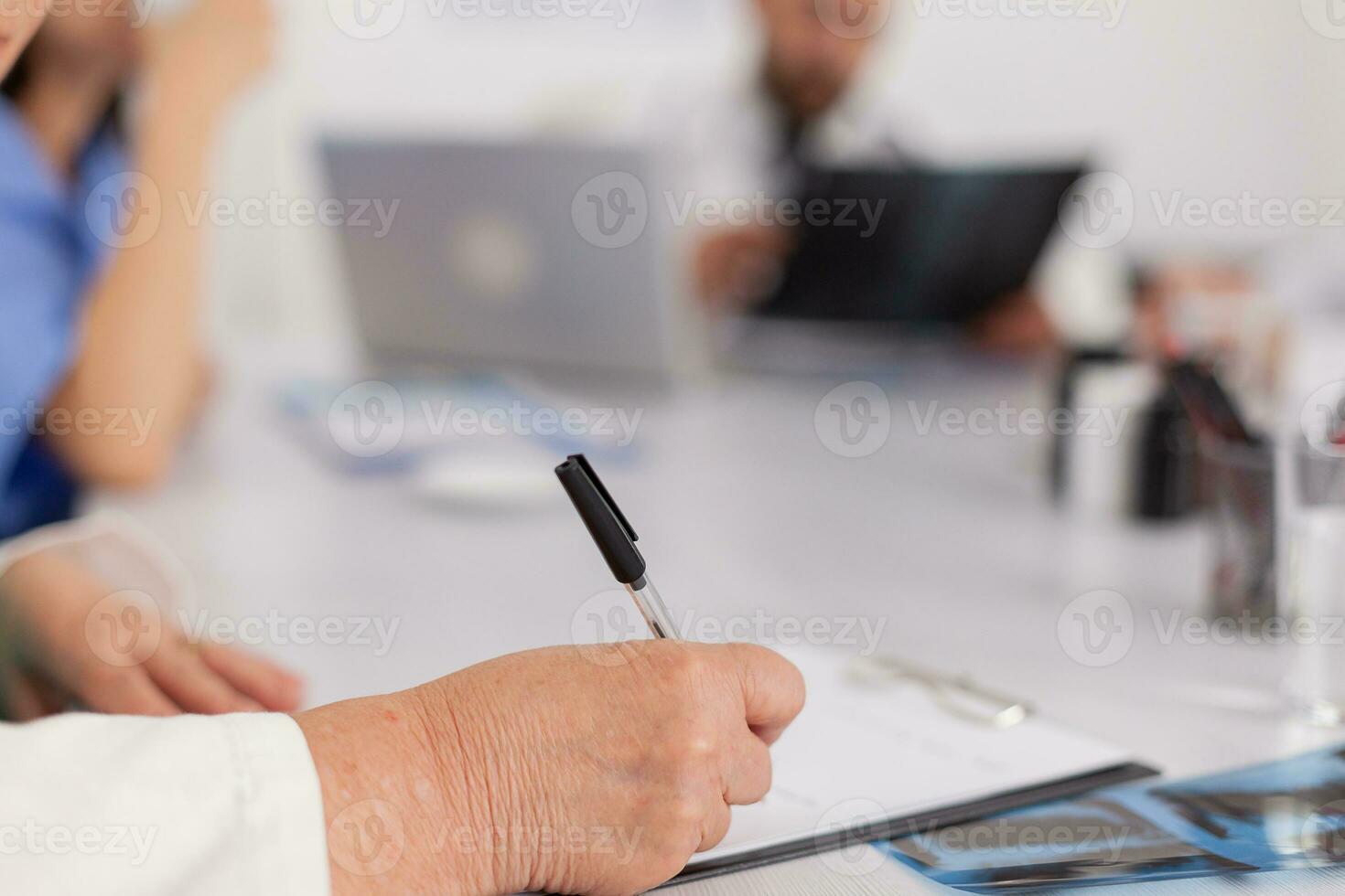 fermer de médecin Sénior femme l'écriture maladie traitement sur presse-papiers prescrire soins de santé pilules des médicaments séance à bureau dans conférence réunion chambre. médecin en cours d'analyse médical compétence photo