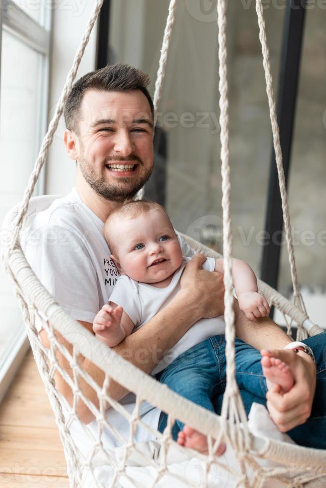 père souriant et heureux tenant sa petite et belle fille assise sur une chaise suspendue photo