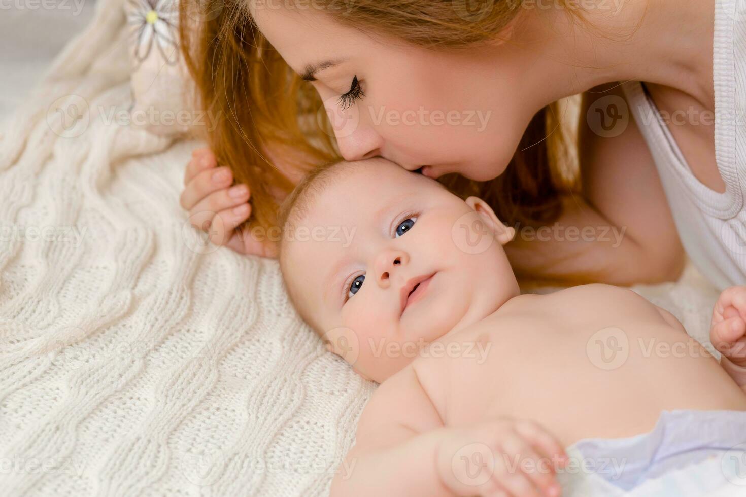 mère et enfant sur une blanc lit. maman et bébé fille dans couche en jouant dans ensoleillé chambre à coucher. photo