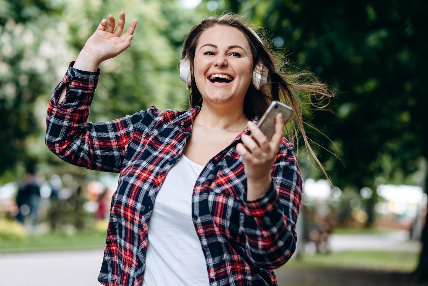 femme en surpoids mignonne, souriante et joyeuse écoutant sa musique préférée avec des écouteurs, au milieu de la rue, à l'extérieur photo