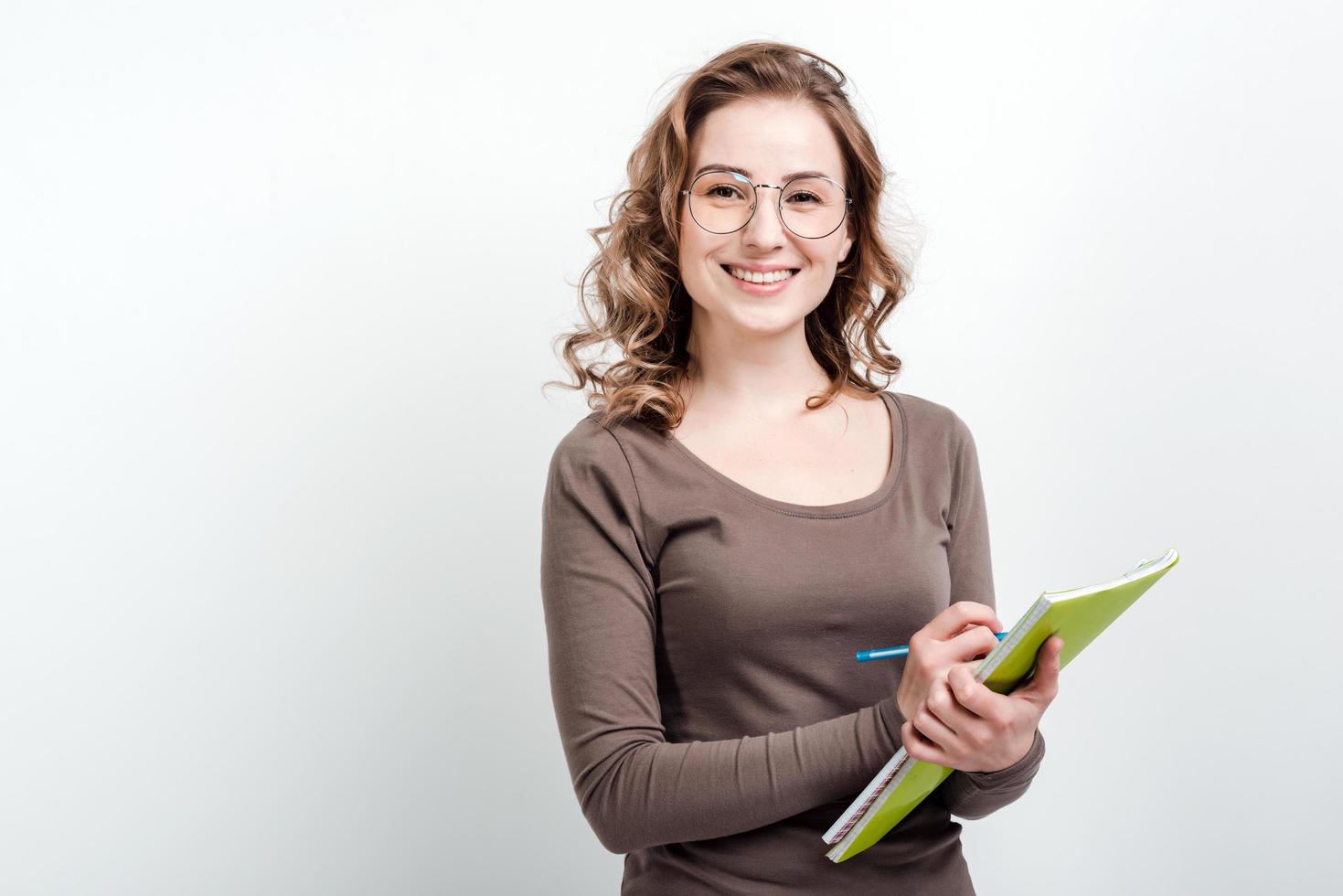 Jolie fille à lunettes prend des notes dans un cahier d'exercices sur fond blanc photo