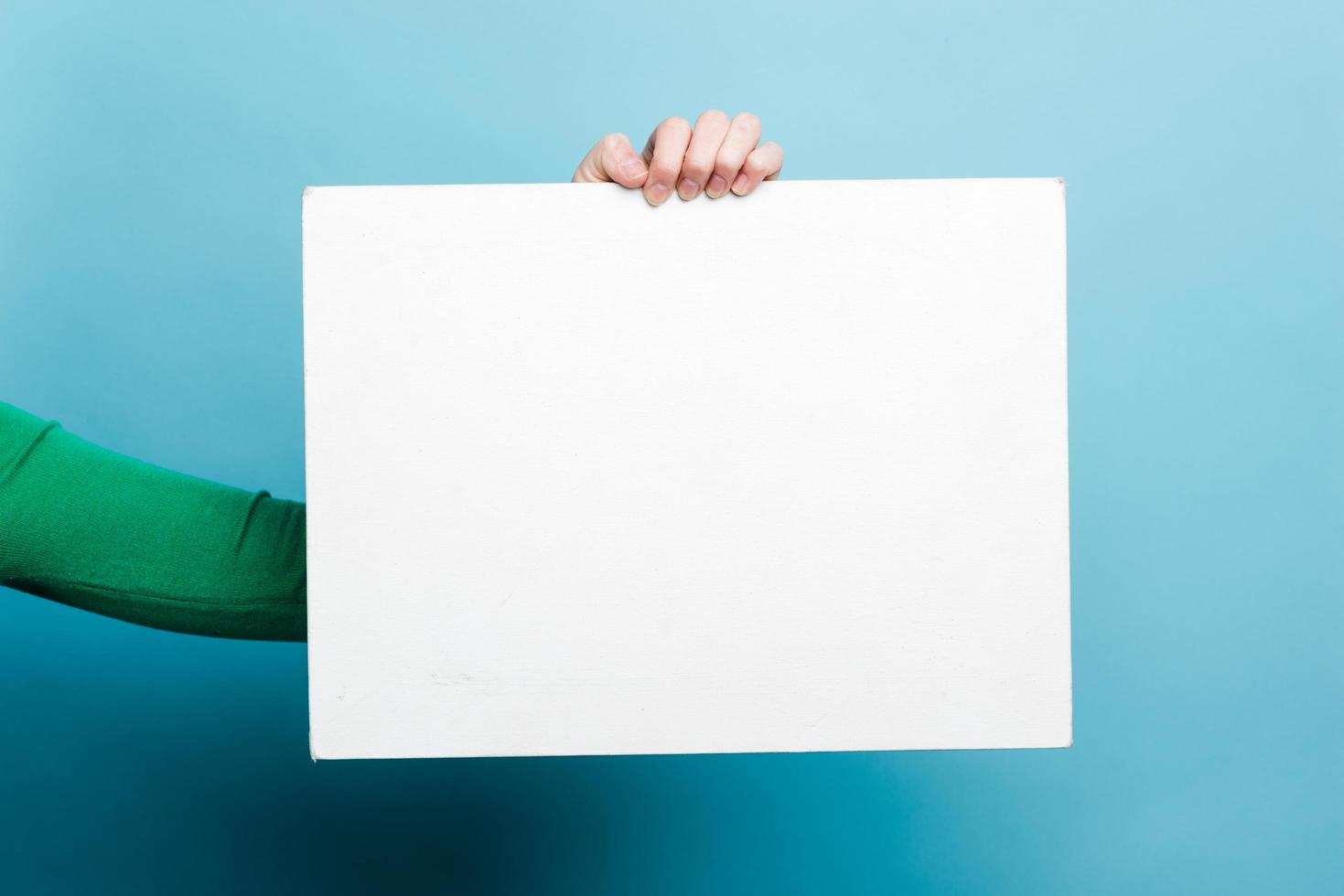 main féminine tenant du papier modèle vide blanc sur fond bleu photo