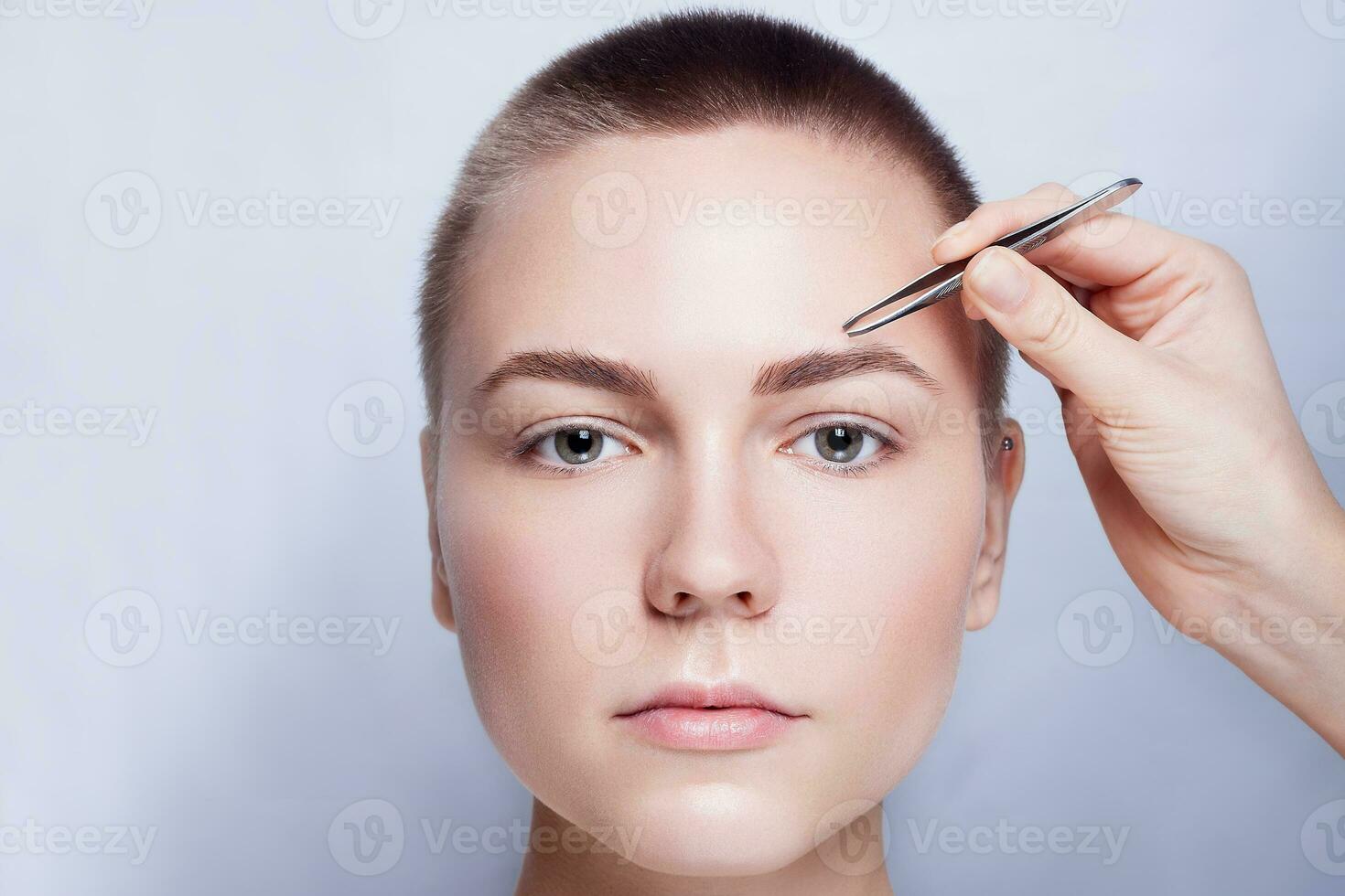 Jeune femme avec court cheveux cueillette les sourcils pince à épiler proche en haut photo