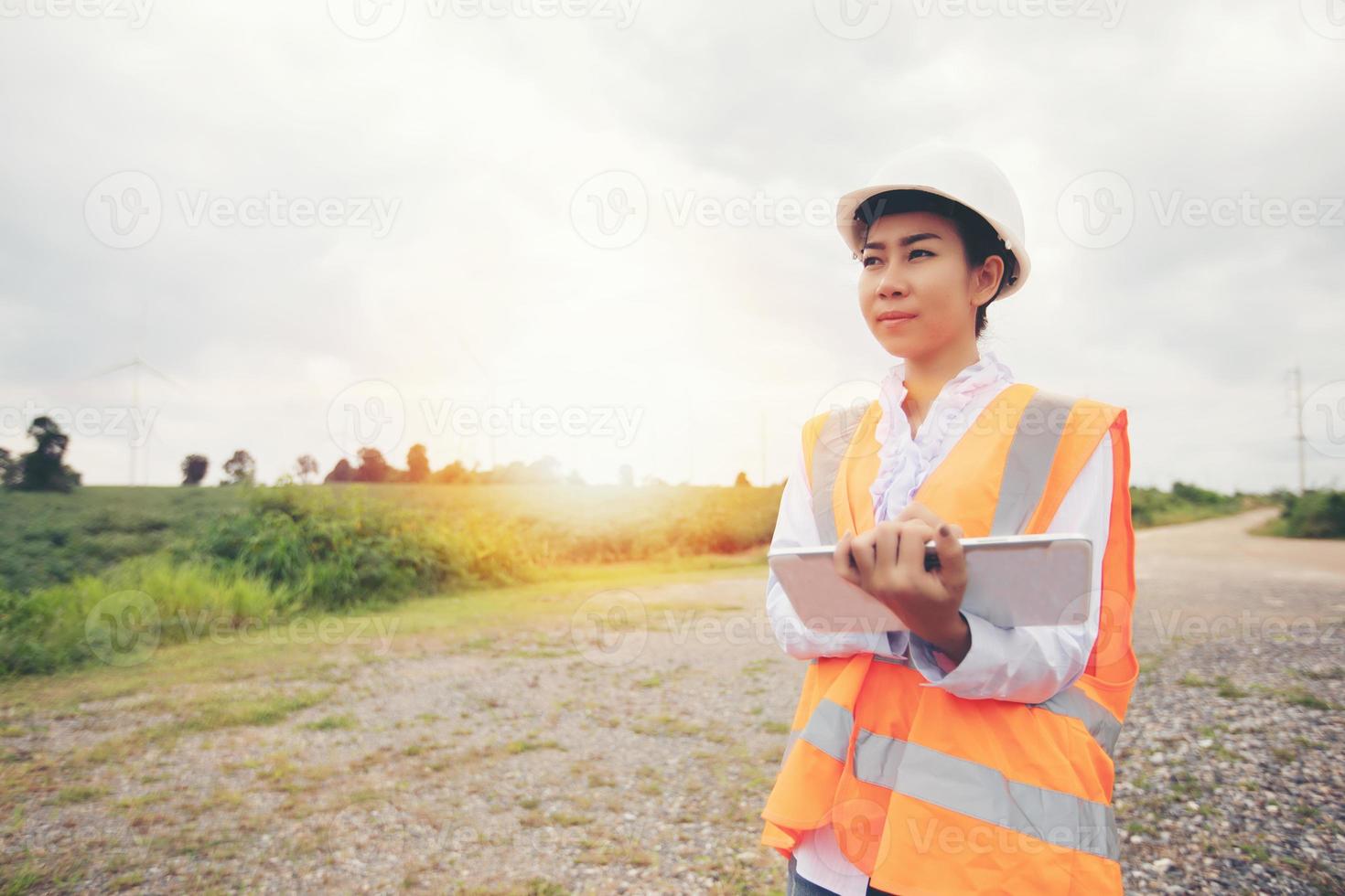 ingénieur asiatique avec casque à l'aide d'un ordinateur tablette inspectant et travaillant à la station de production d'électricité du parc d'éoliennes photo