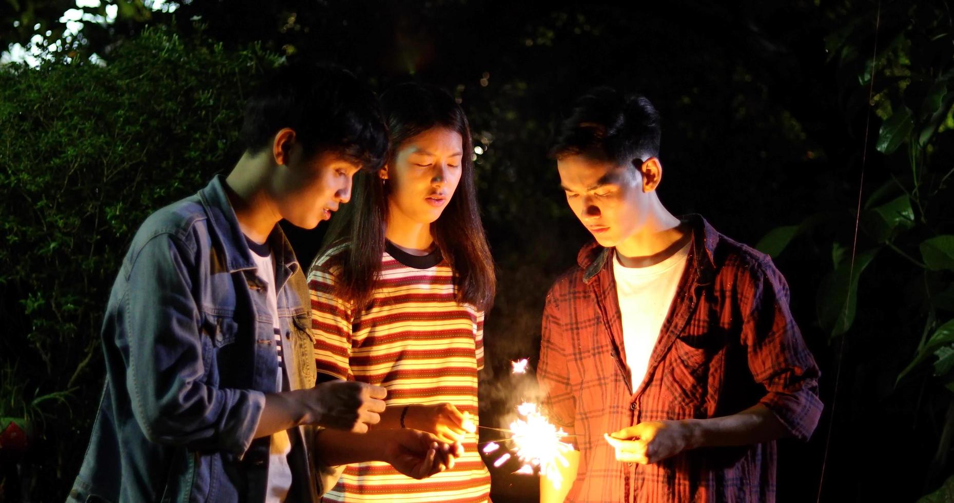 groupe d'amis asiatiques ayant un barbecue de jardin en plein air riant avec des boissons à la bière alcoolisées et montrant un groupe d'amis s'amusant avec des cierges magiques la nuit, mise au point douce photo