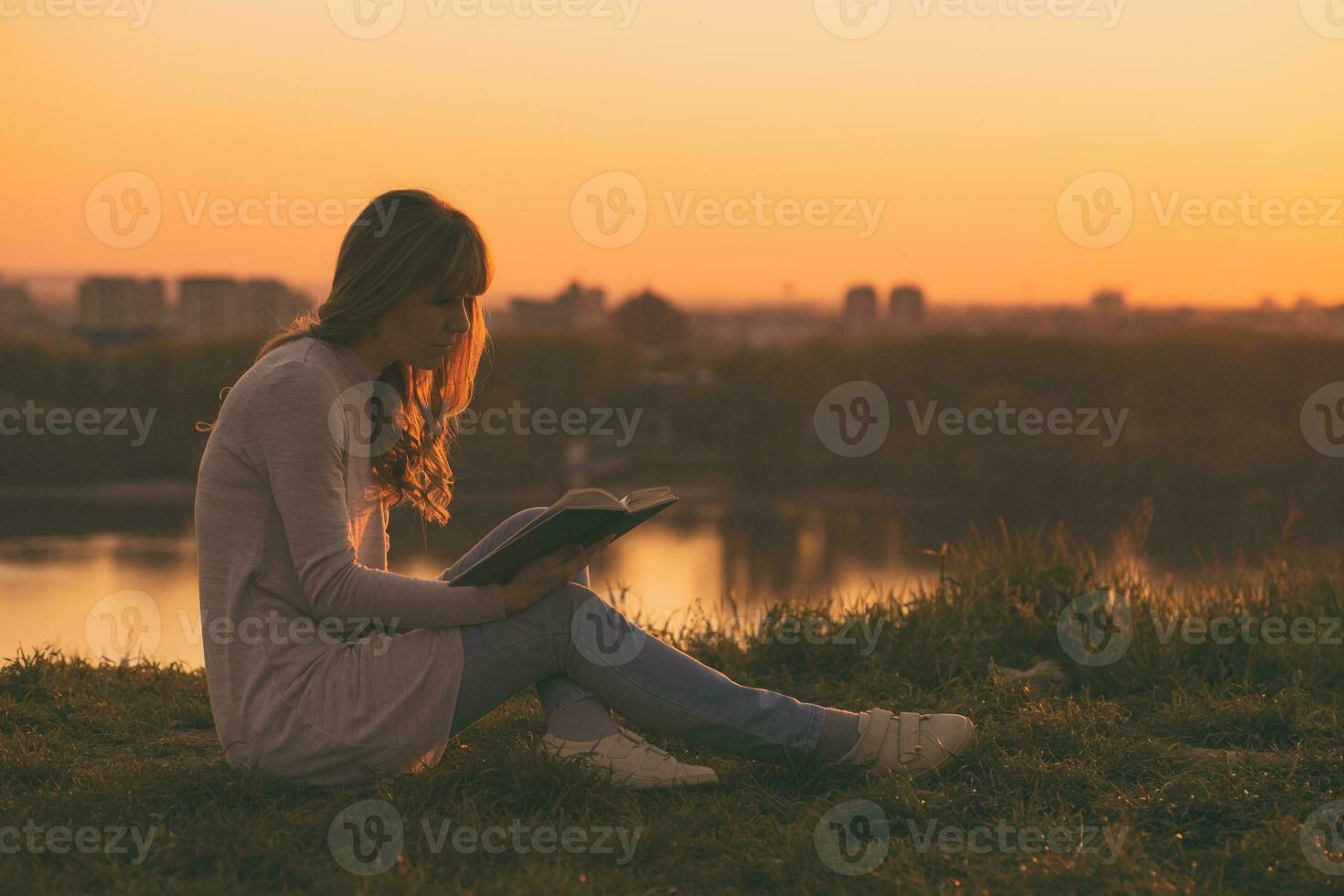 femme jouit en train de lire une livre avec une le coucher du soleil plus de le ville. photo