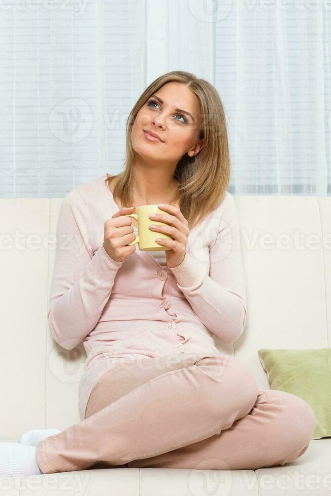 magnifique femme est en portant tasse et relaxant à sa Accueil sur canapé photo