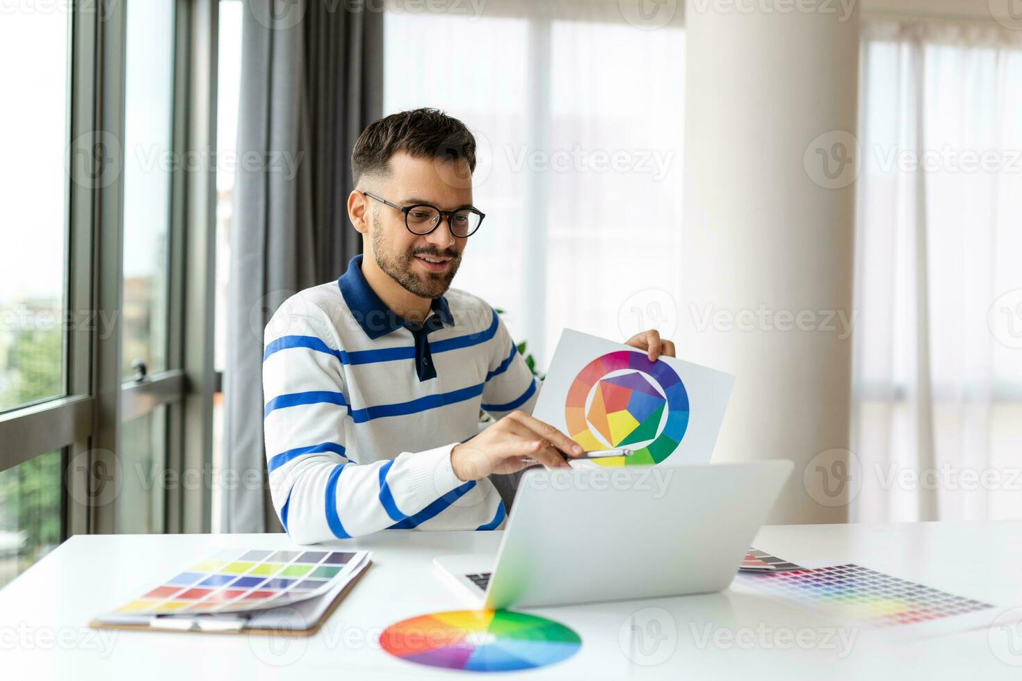 Jeune free-lance graphique designer gars travail avec portable et Couleur échantillons, séance à bureau dans Accueil bureau, choisir Couleur gamma pour Nouveau conception projet, côté vue avec copie espace photo