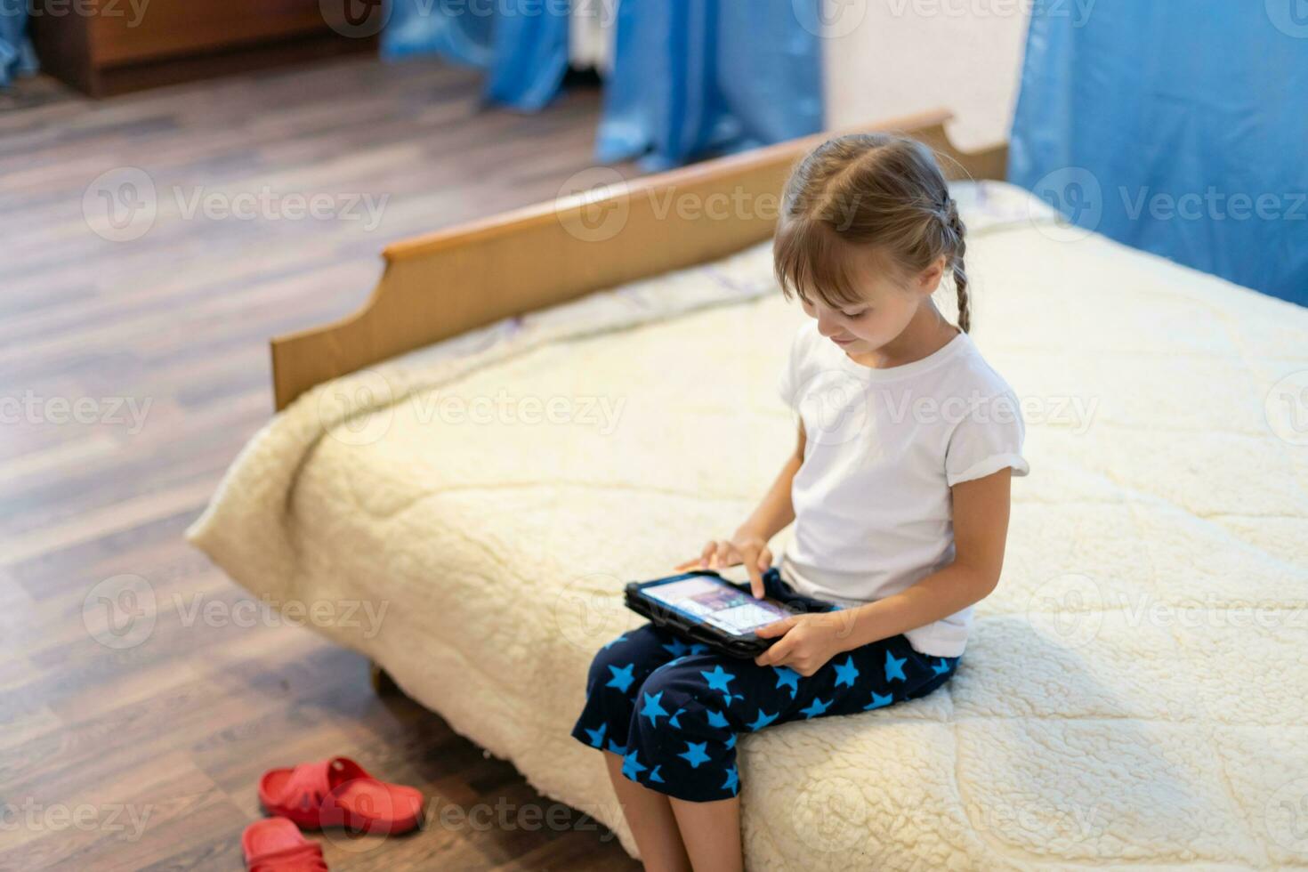 portrait de la mignonne peu fille en jouant sur numérique tablette tandis que séance à Accueil dans vivant chambre. photo