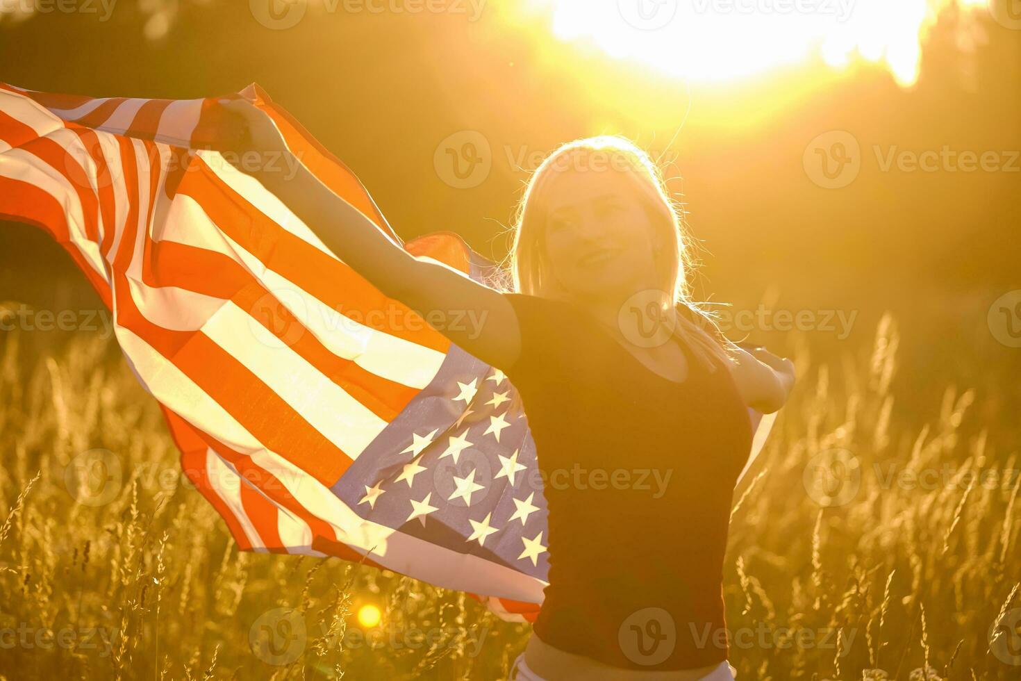 magnifique Jeune fille en portant un américain drapeau dans le vent dans une champ de seigle. été paysage contre le bleu ciel. horizontal orientation. photo