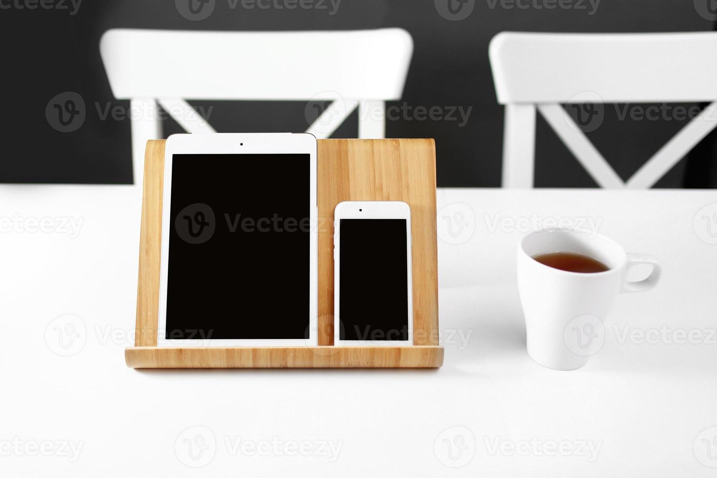 une tablette blanche et un smartphone sur un support sur un lieu de travail de bureau de table blanche. une tasse de thé sur le lieu de travail photo