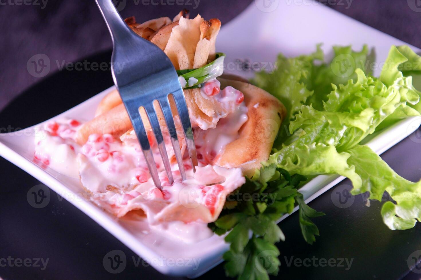 crêpe avec rouge caviar et Mayonnaise fabriqué dans une sac lié avec vert oignons sur une blanc carré assiette persil salade feuilles ukrainien slave nourriture photo