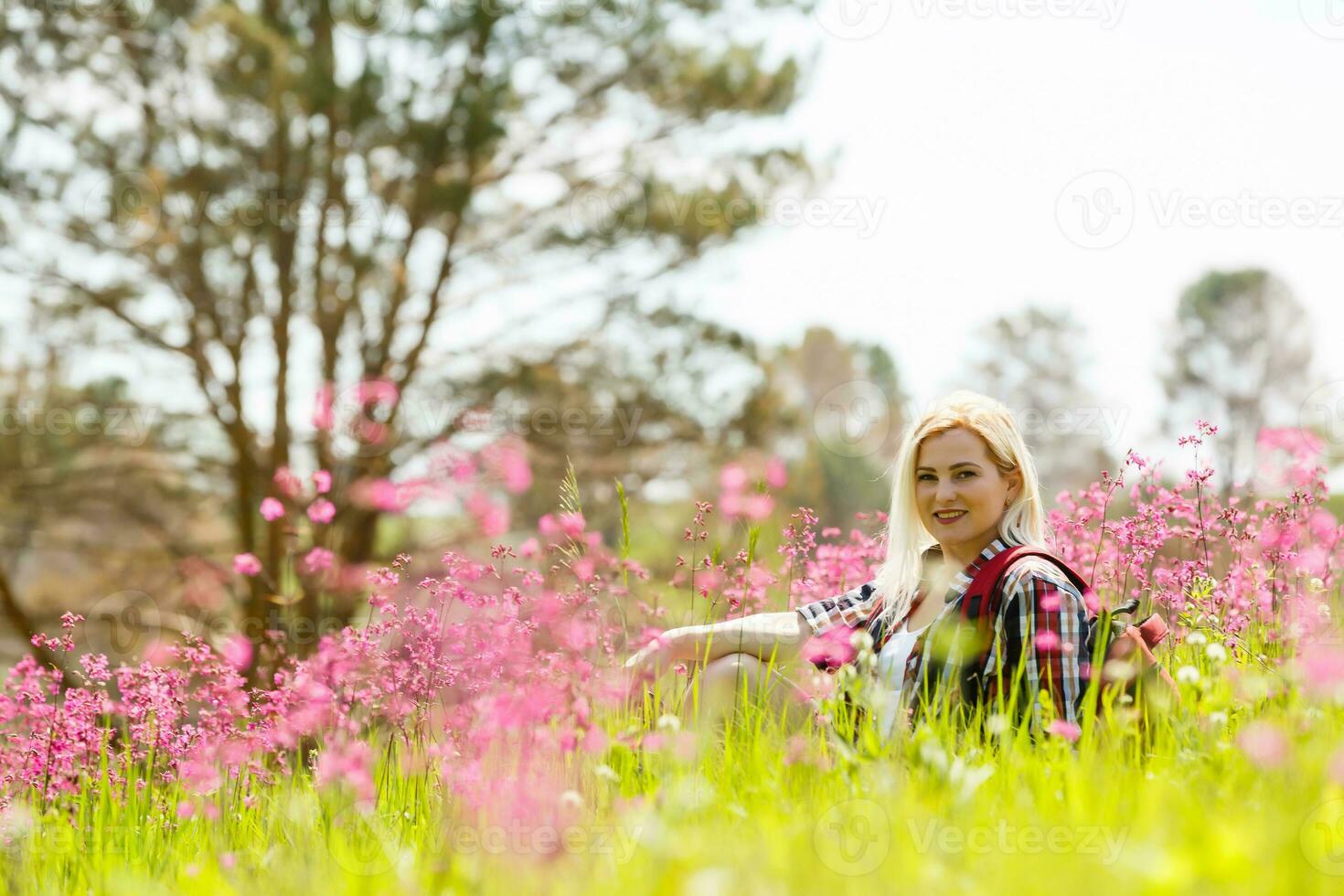 content aventurier femelle des stands sur le vert Montagne pente parmi floraison rose rhododendrons et à la recherche dans le distance. épique Voyage dans le montagnes. large angle. photo