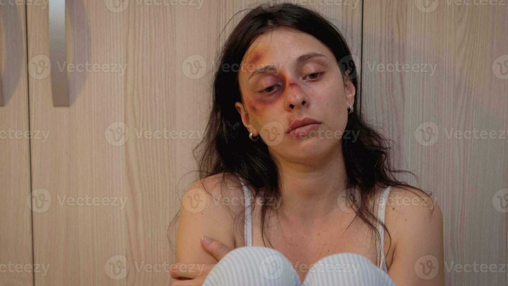 visage de le femme victime de la violence séance sur le sol tremblant. traumatisé abusé terrifié battu épouse couvert dans ecchymoses Souffrance blessure de alcoolique agression brutal ivre homme. photo