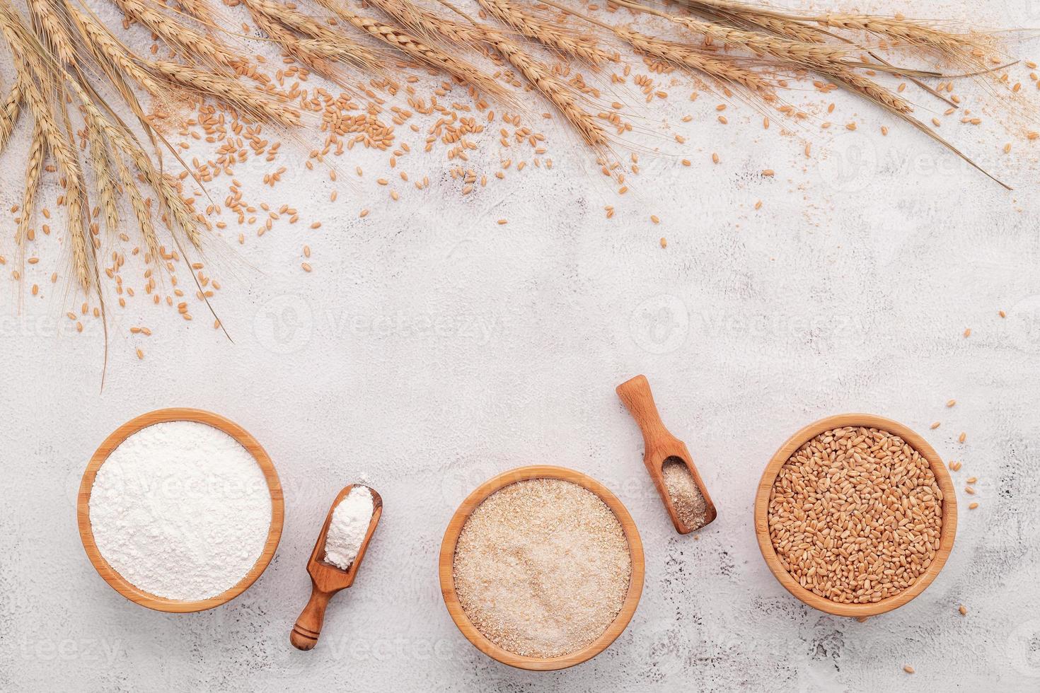 grains de blé, farine de blé brun et farine de blé blanc dans un bol en bois mis en place sur fond de béton blanc. photo