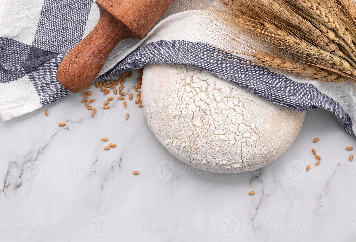 pâte à levure fraîche faite maison reposant sur une table en marbre avec des épis de blé et un rouleau à pâtisserie. photo