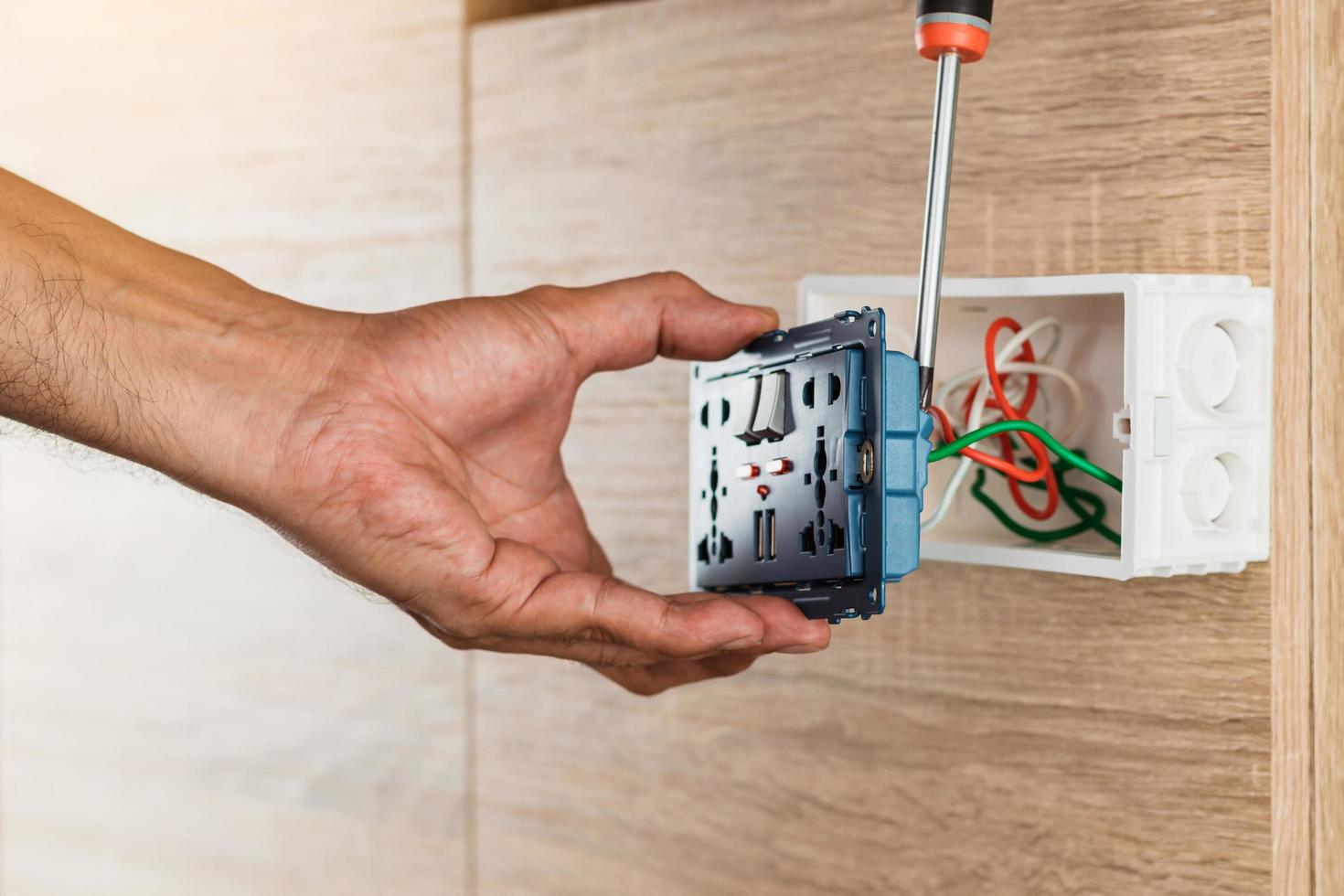 la main d'un électricien utilise un tournevis pour attacher les fils à la prise d'alimentation murale universelle avec port USB et marche-arrêt dans une boîte en plastique sur un mur en bois. photo