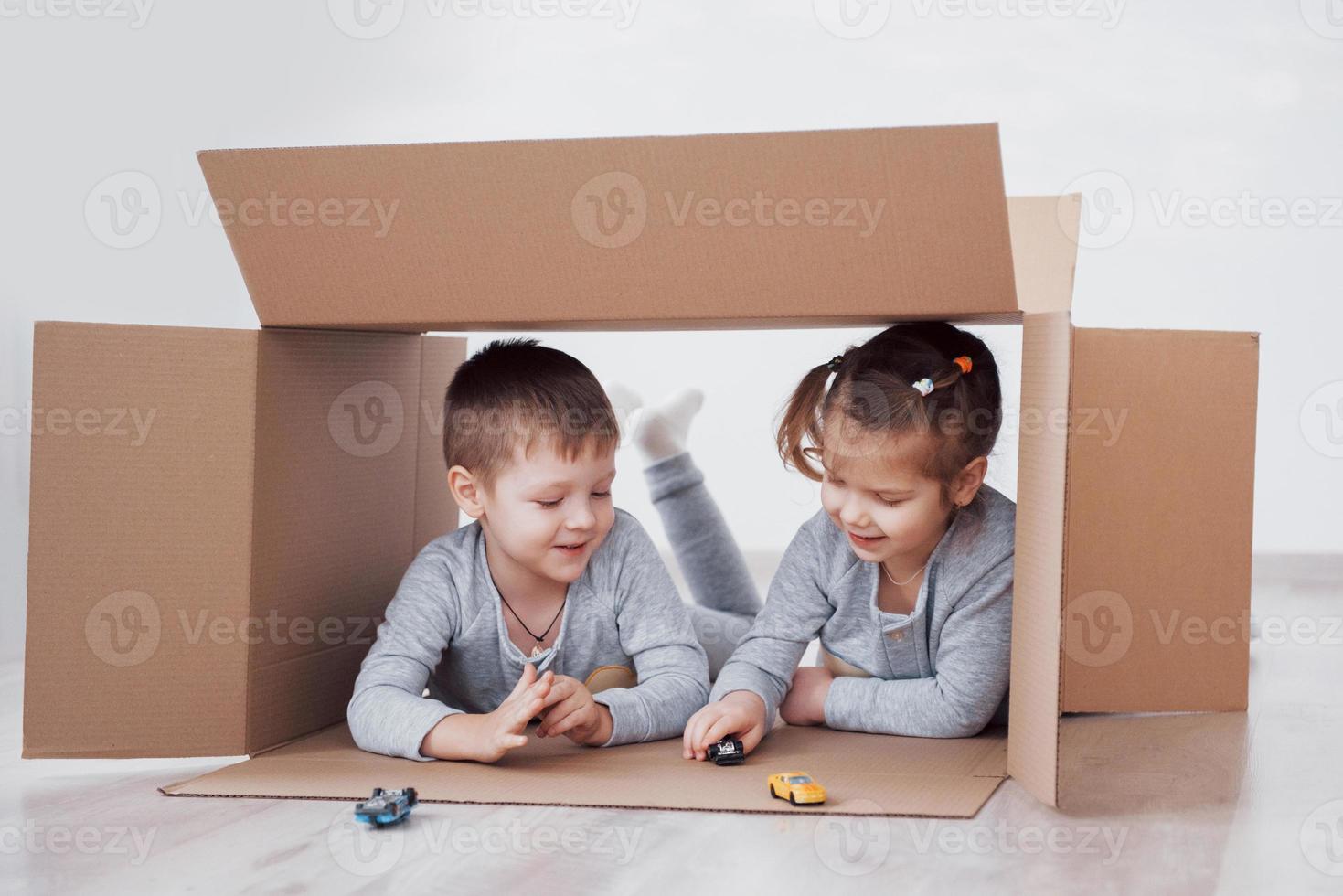 deux un petit garçon et une fille jouant de petites voitures dans des boîtes en carton. photo conceptuelle. les enfants s'amusent. photo conceptuelle. les enfants s'amusent