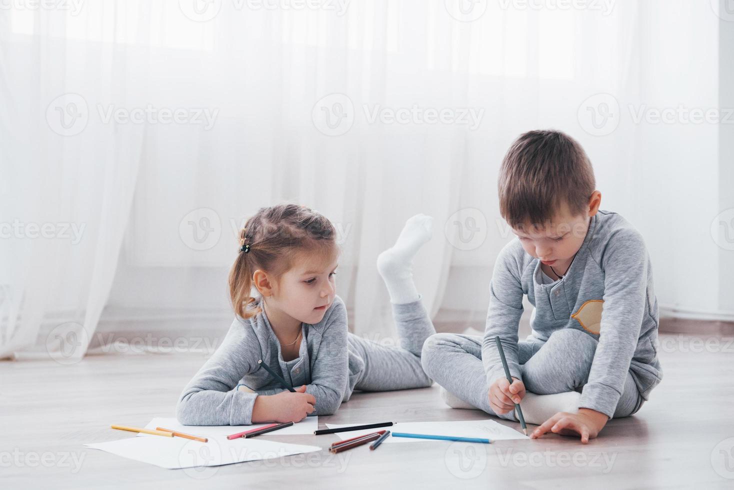 les enfants sont allongés par terre en pyjama et dessinent avec des crayons. peinture d'enfant mignon par des crayons photo