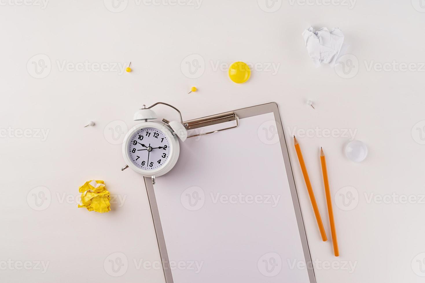 papier vierge sur presse-papiers, réveil blanc et vue de dessus de papeterie sur fond blanc photo