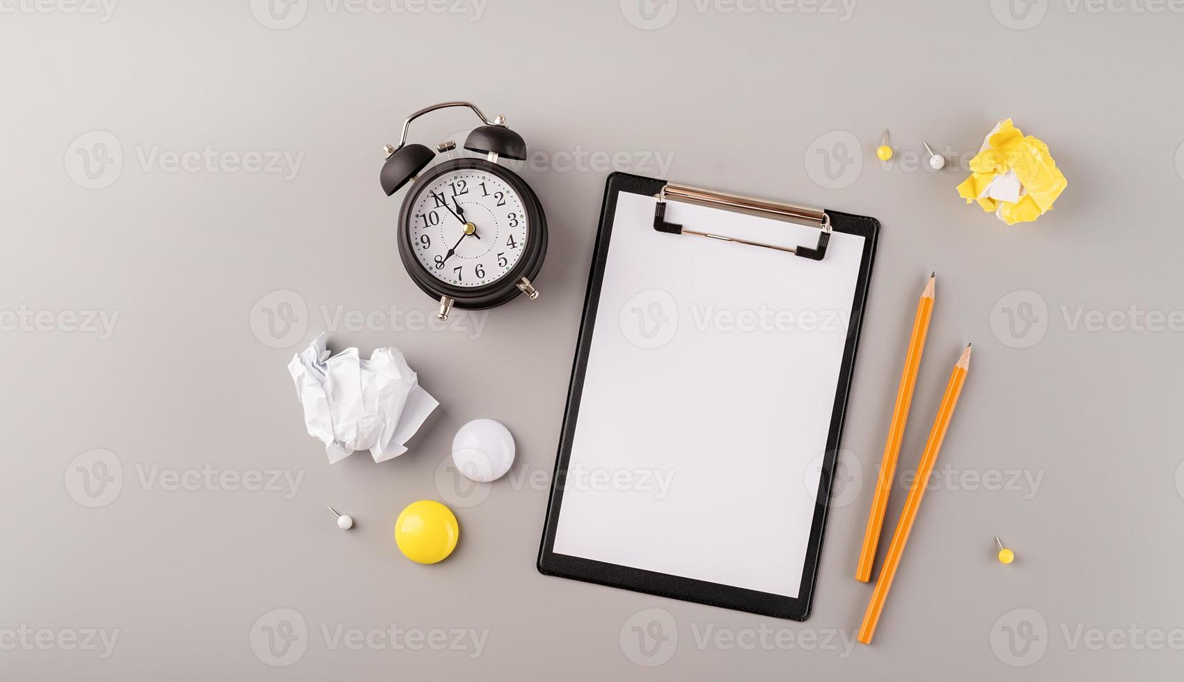 papier vierge sur presse-papiers, réveil blanc et vue de dessus de la papeterie sur fond gris photo