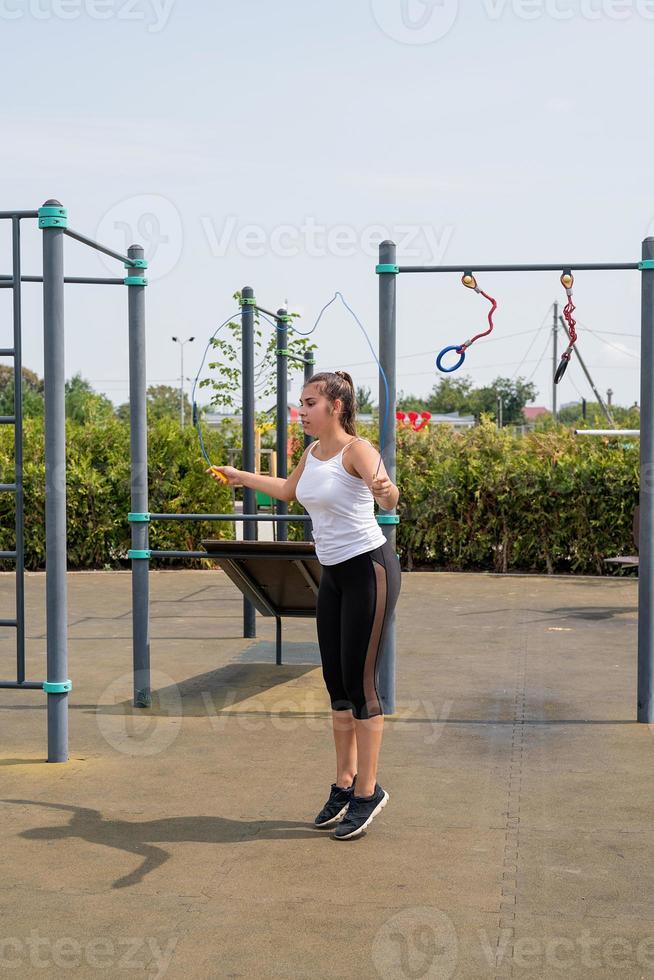 femme heureuse travaillant sur le terrain de sport en journée d'été ensoleillée à la corde à sauter photo