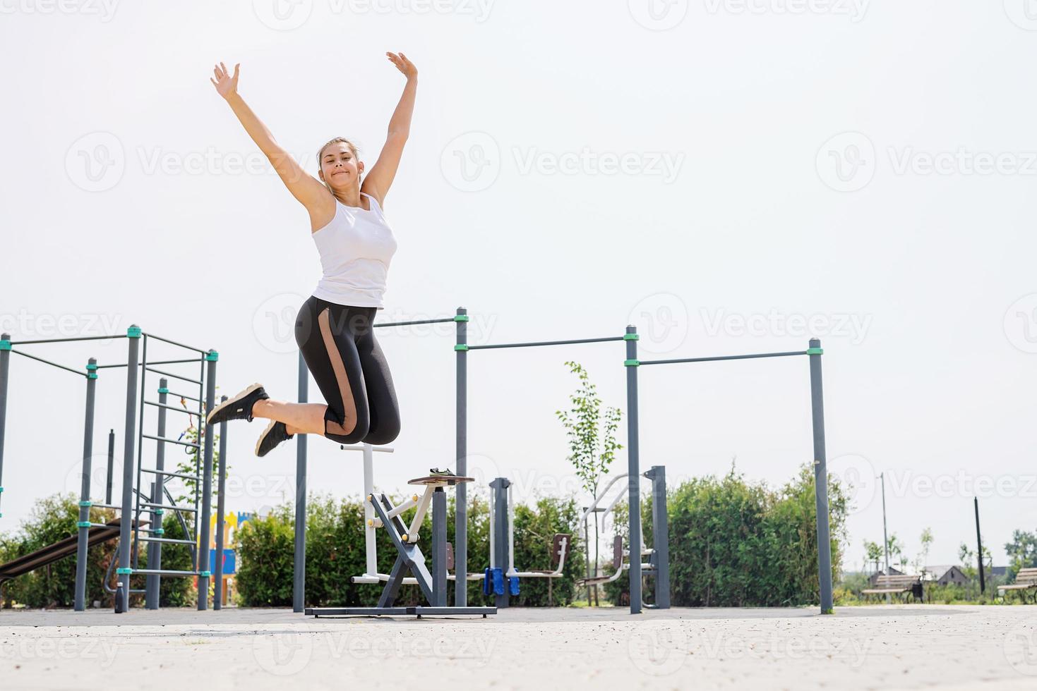 femme heureuse sautant sur le terrain de sport en journée d'été ensoleillée, levant les bras, profitant du soleil photo