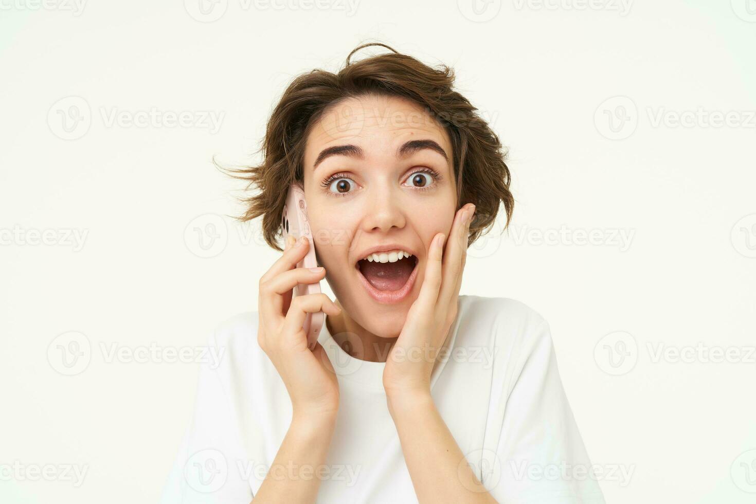 portrait de femme avec surpris affronter, réponses téléphone appel et regards excité, étonné par gros nouvelles, des stands plus de blanc Contexte photo