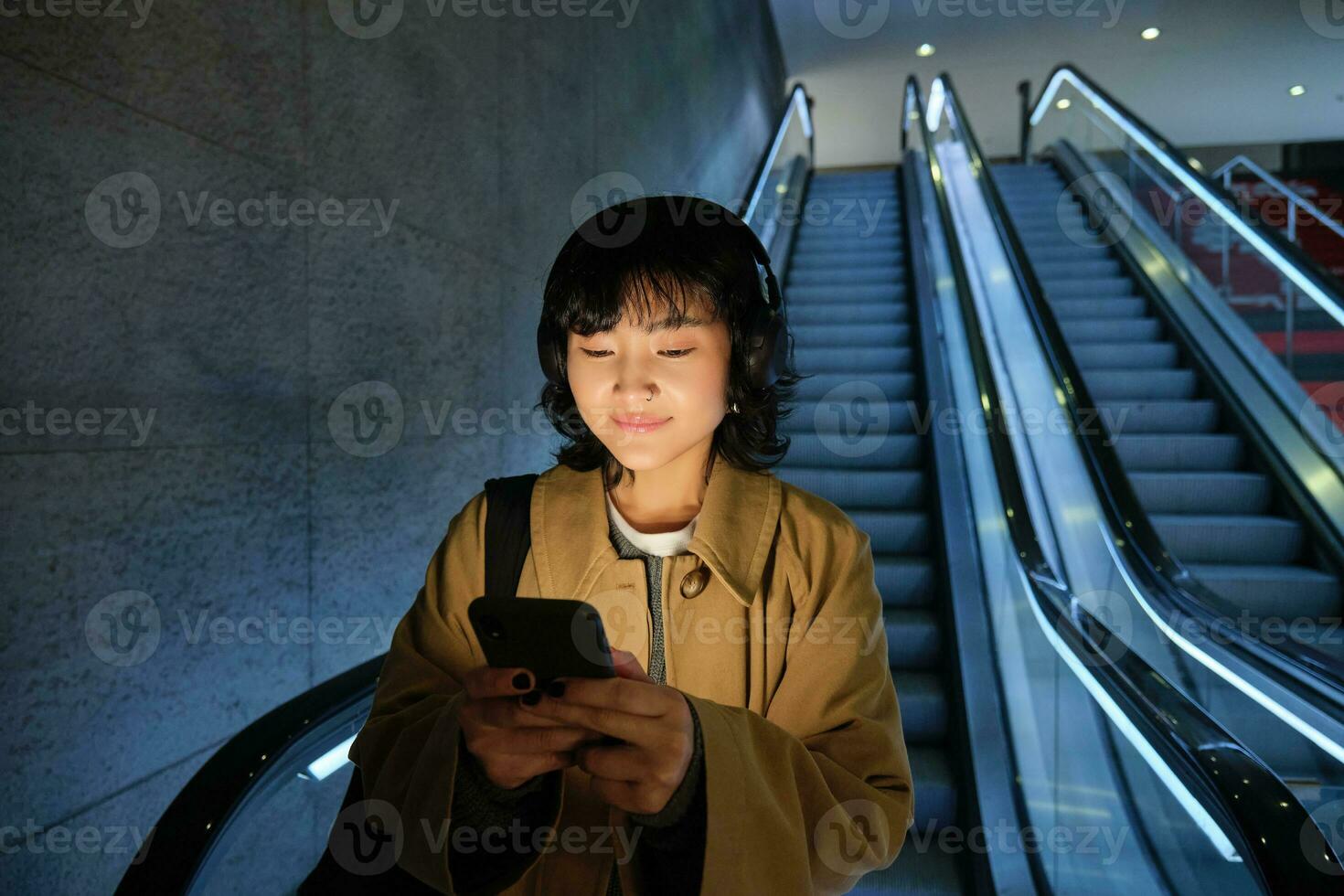 mignonne Jeune femme Aller vers le bas le escalier mécanique à le tube, en utilisant métro métro à commuer à travail ou université, permanent avec téléphone intelligent photo