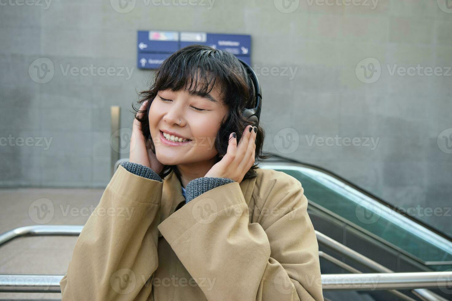 portrait de content femme, coréen fille dans écouteurs, écoute la musique dans écouteurs, profiter du son de écouteurs, en riant et souriant photo