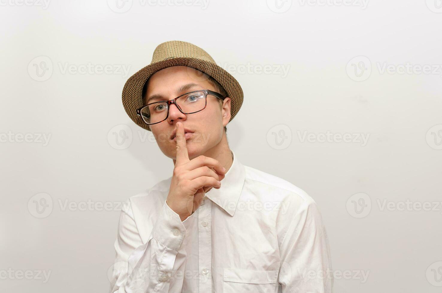 Jeune gars dans des lunettes et une chapeau pressé une doigt à le sien bouche. photo