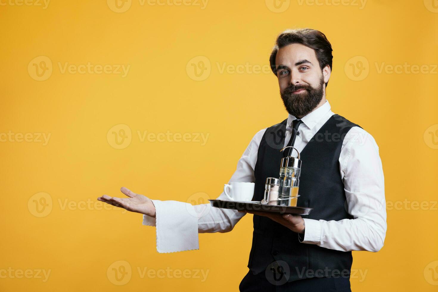 professionnel serveur en présentant quelque chose dans studio, fournir luxueux un service à restaurant tandis que il porte plat avec coutellerie et café. Masculin majordome portion les boissons à clients, bien à manger. photo