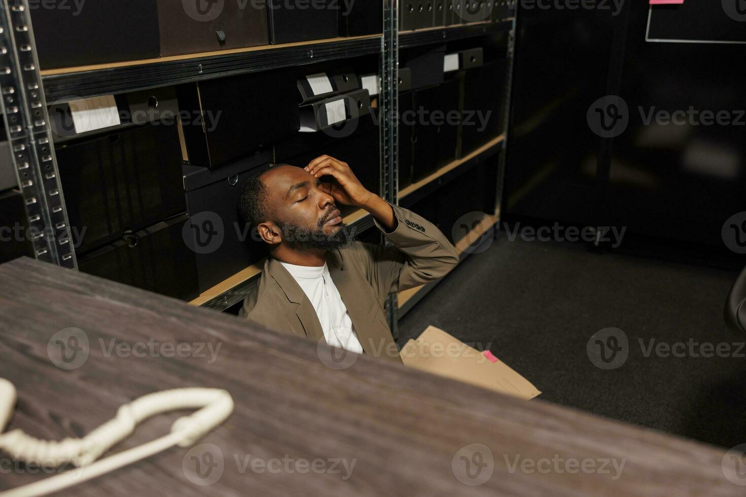 stressé flic séance sur sol fermeture yeux et résolution la criminalité dans police Bureau à nuit temps. fatigué somnolent africain américain enquêteur conduite enquête et en cours d'analyse des indices photo