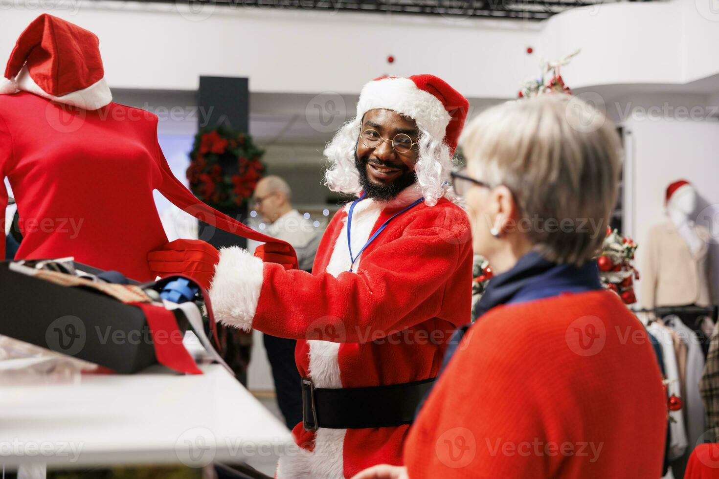 boutique employé guidage client dans boutique, portant de fête Père Noël claus costume tandis que portion les clients avec Noël présent des idées et suggestions. Jeune homme recommander chemisier à Sénior femme. photo