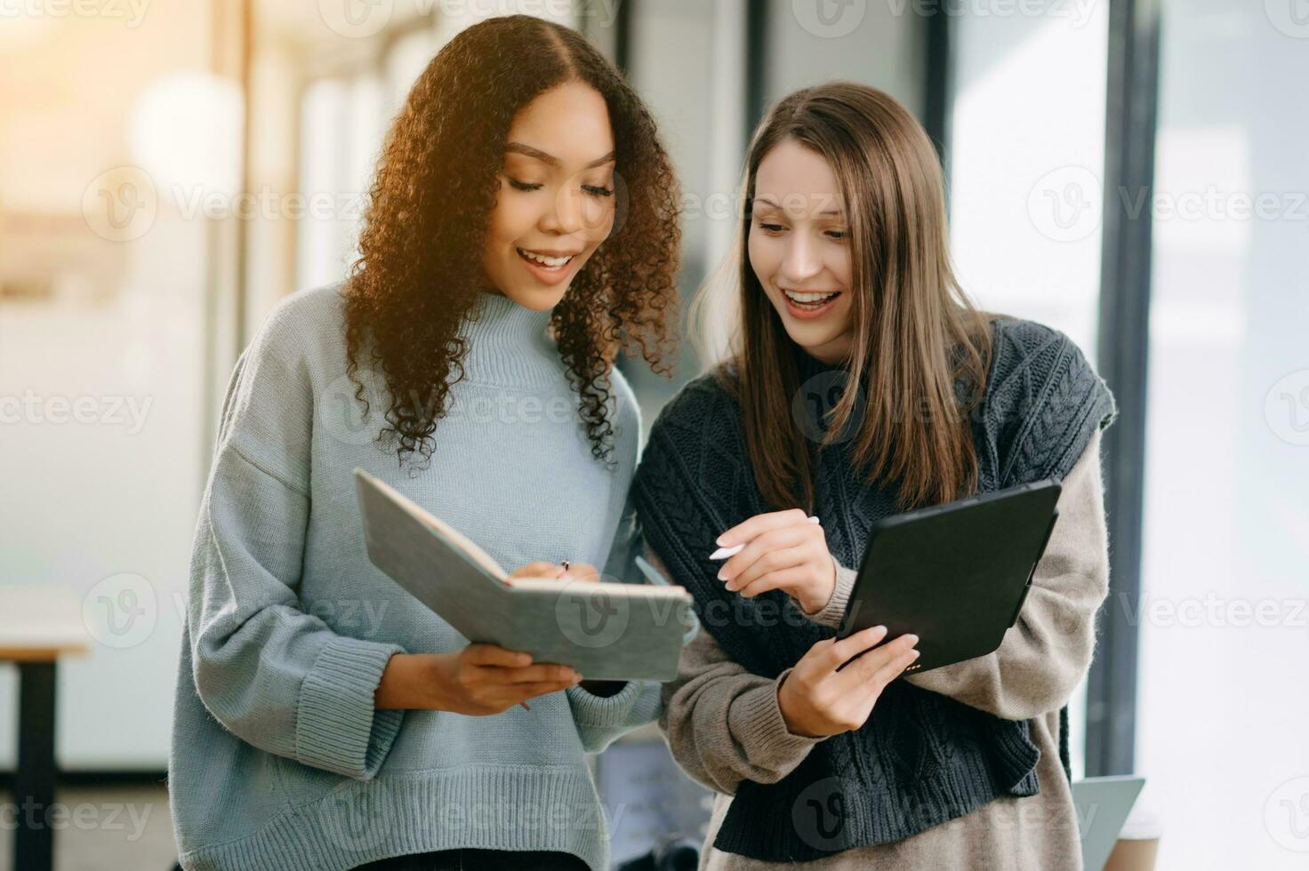 deux attrayant Jeune femelle Université élèves travail sur le école projet en utilisant ordinateur et tablette ensemble, prendre plaisir parlant et écouteurs ayant une vidéo discuter. photo