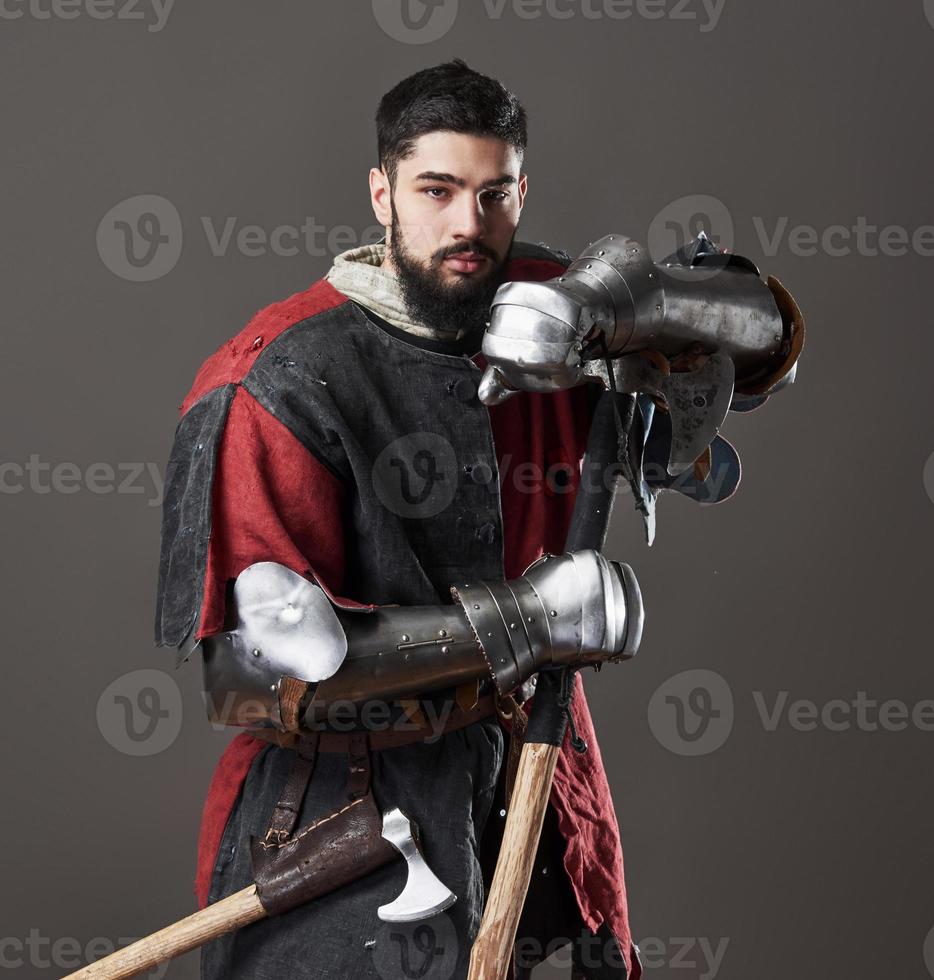 chevalier médiéval sur fond gris. portrait d'un guerrier brutal au visage sale avec une armure de cotte de mailles, des vêtements rouges et noirs et une hache de combat photo