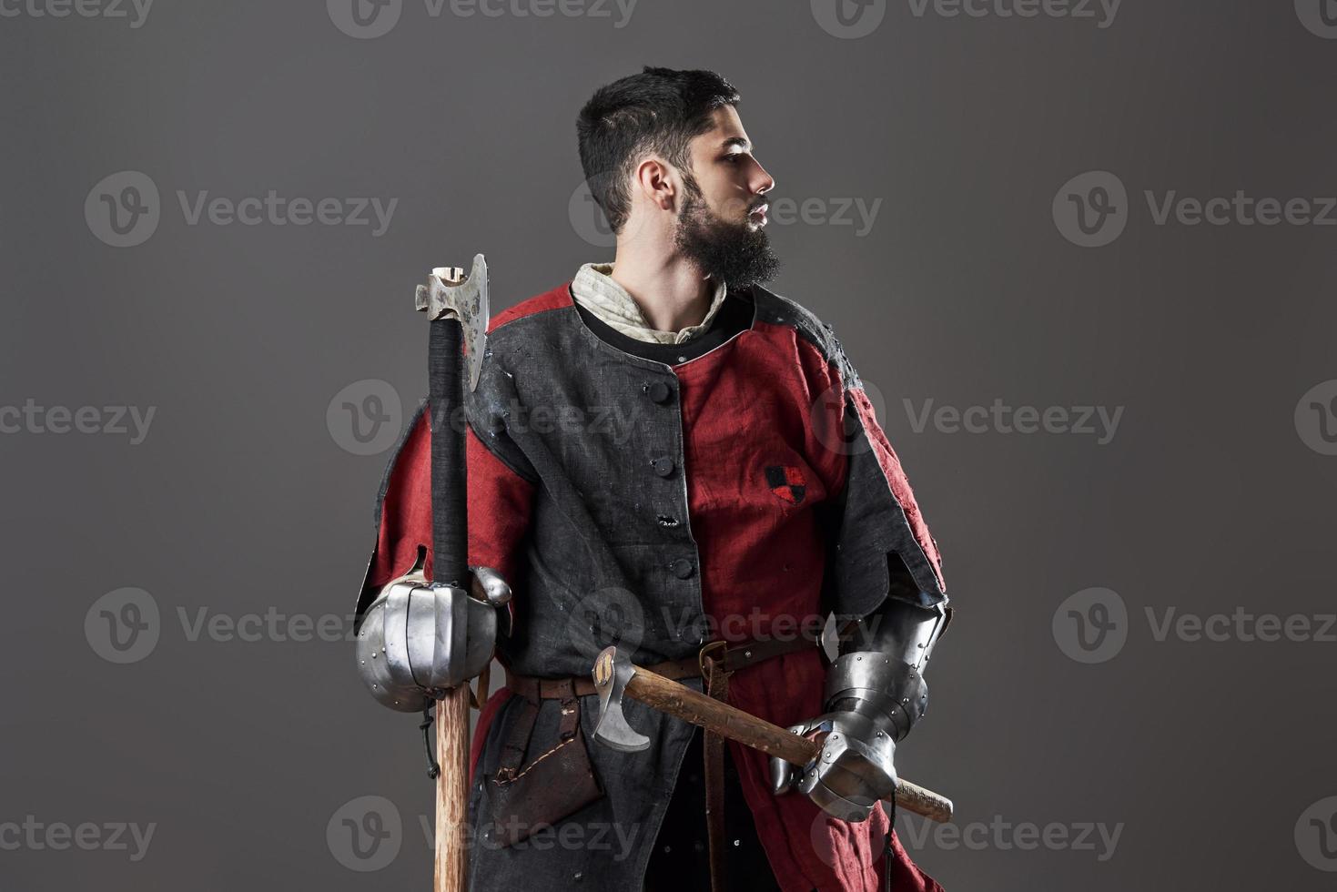 chevalier médiéval sur fond gris. portrait d'un guerrier brutal au visage sale avec une armure de cotte de mailles, des vêtements rouges et noirs et une hache de combat photo