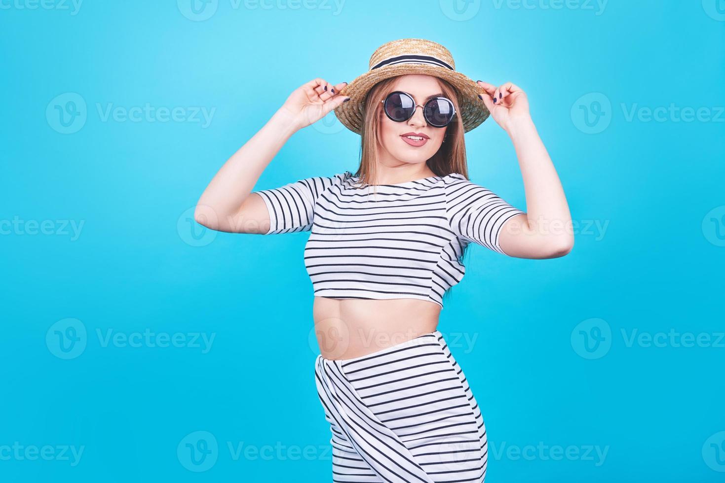 jolie fille à rayures blanches et noires, chapeau, lunettes de soleil, bouche ouverte émotionnellement sur fond bleu vif avec un corps parfait. isolé. prise de vue en studio photo